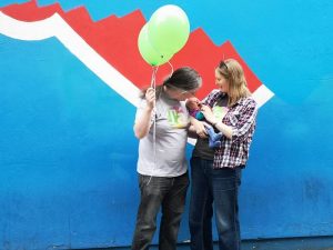 Photograph of Helen Stonehouse, her partner and baby, with balloons ,in front of the partial Repeal mural. 