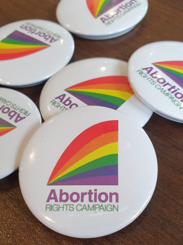 a handful of badges with the ARC logo in pride colours