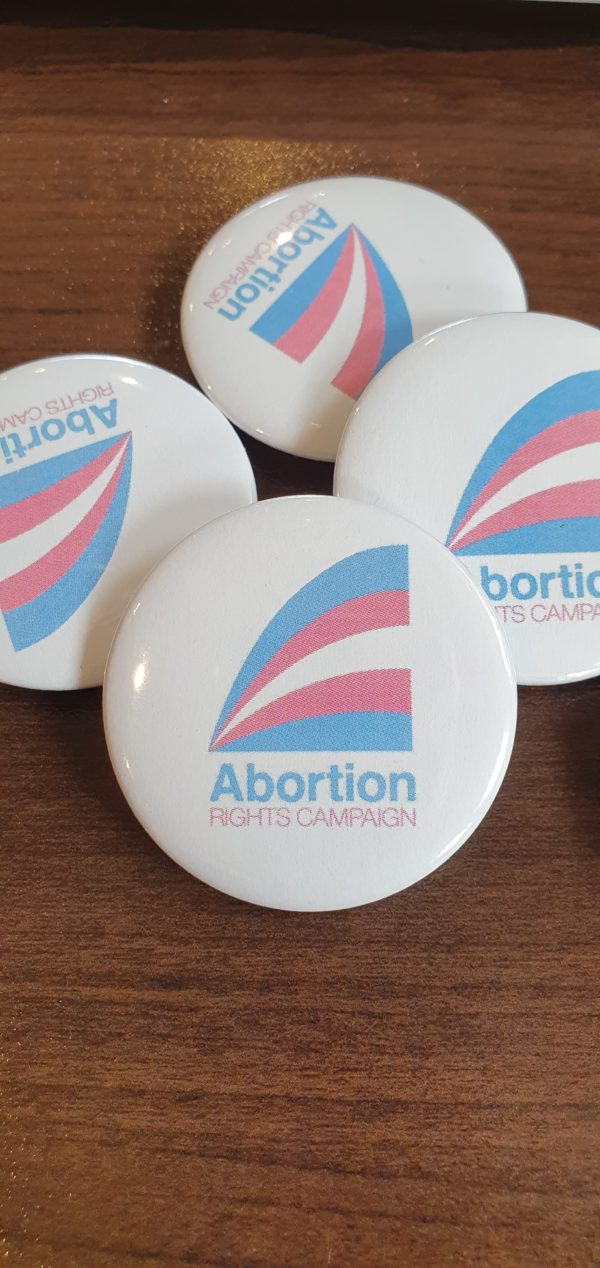 a handful of badges with the ARC logo in Trans pride colours