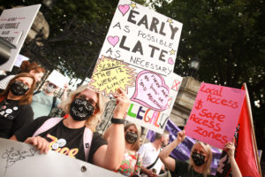 Protesters at the Abortion Rights Campaign March for Choice in 2021 outside Leinster House. The people are holding handmade posters that say 'As Early As Possible As Late As Necessary', 'Scrap the 12 week limit! There are no 'good' or 'bad' abortions' and 'Local Access and Safe Access Zones'